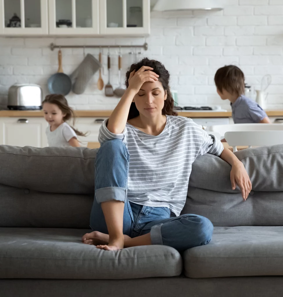 stressed Mom sitting on couch with running children in background